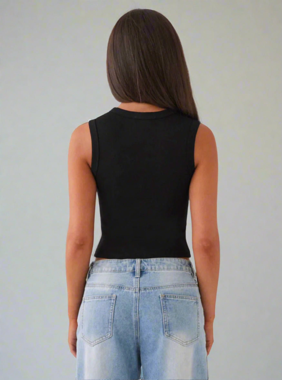 Person wearing a black sleeveless top and light blue jeans against a plain background