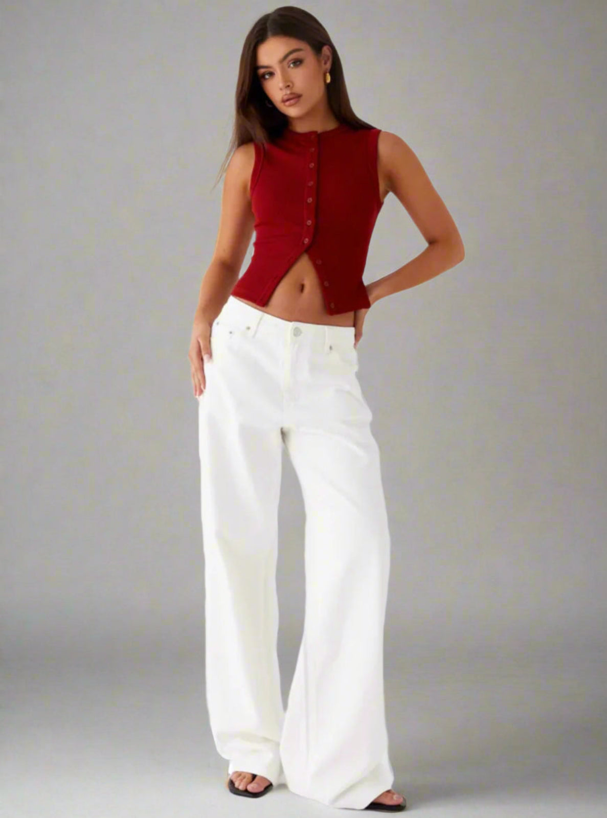 Woman wearing a red sleeveless top and white pants against a gray background