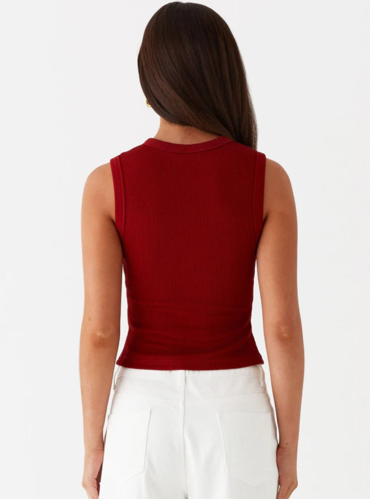 Person wearing a red sleeveless top and white pants on a white background
