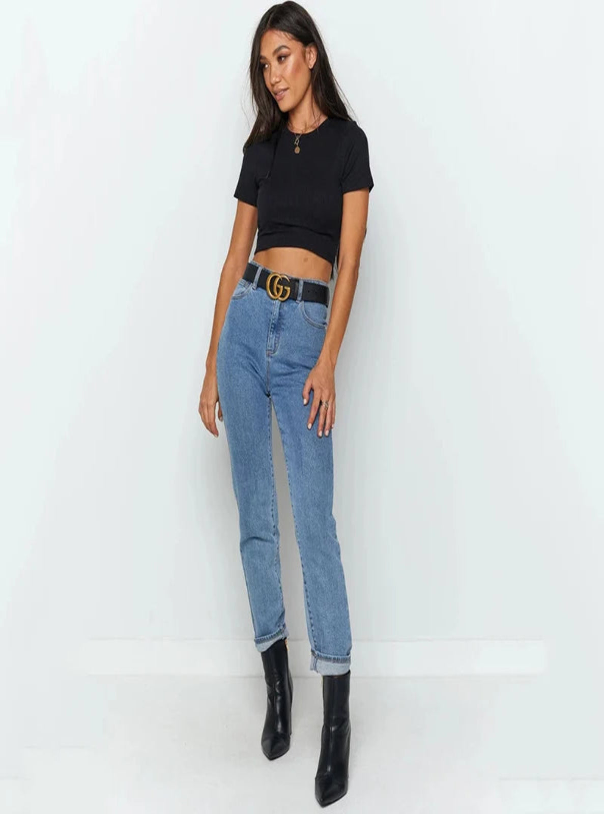 Woman wearing a black crop top, blue jeans, and black boots on a white background
