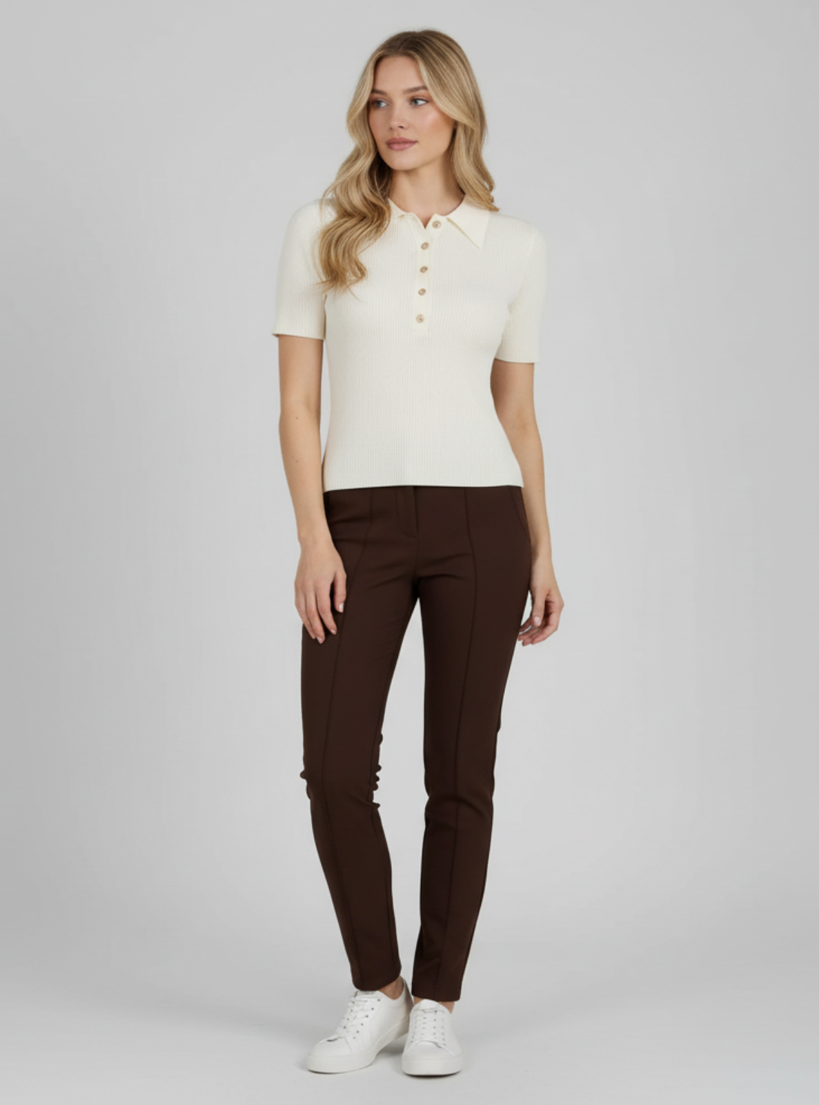 Woman wearing a white polo shirt and brown pants on a gray background