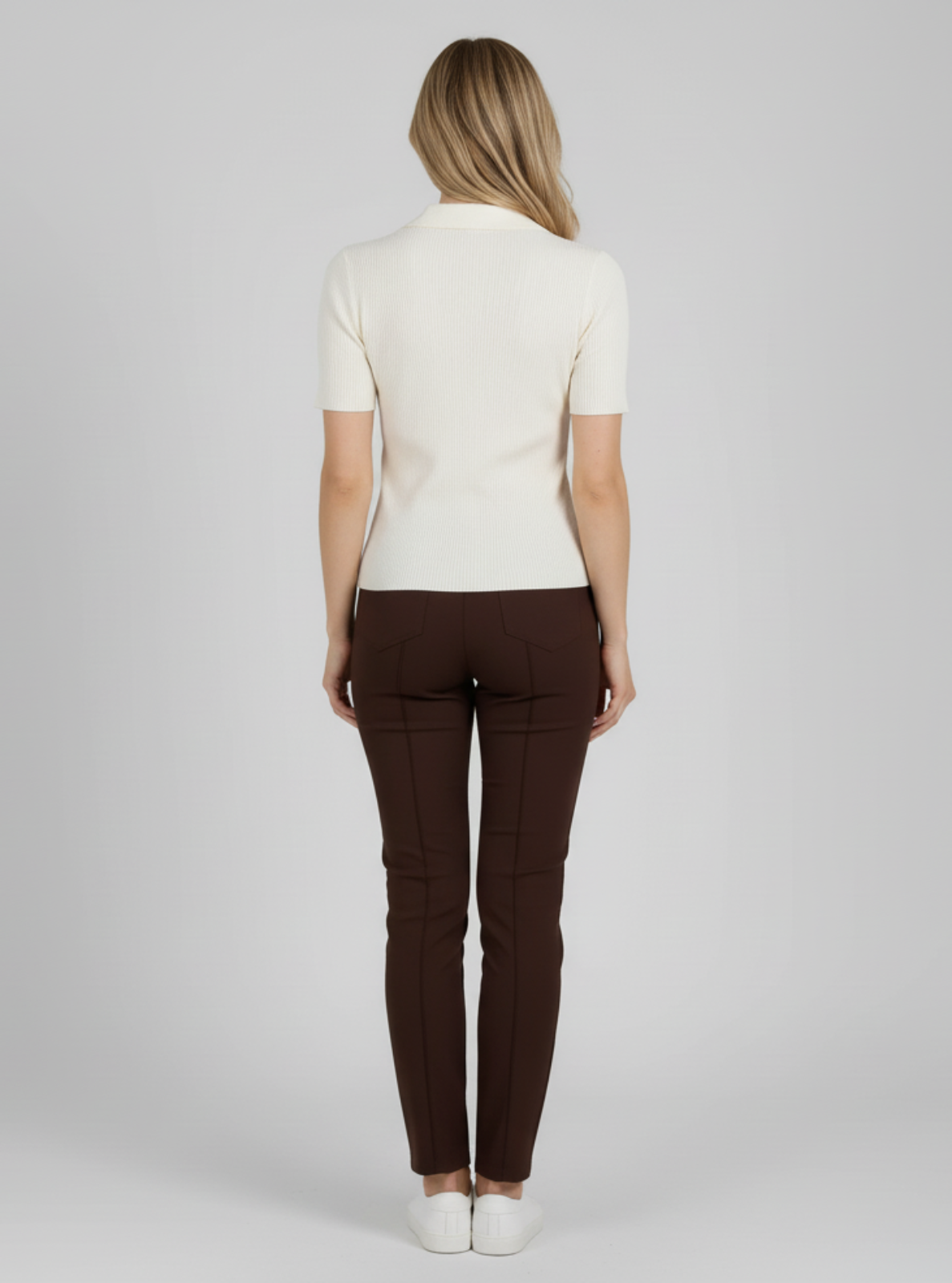 Woman wearing a white top and brown pants on a plain background