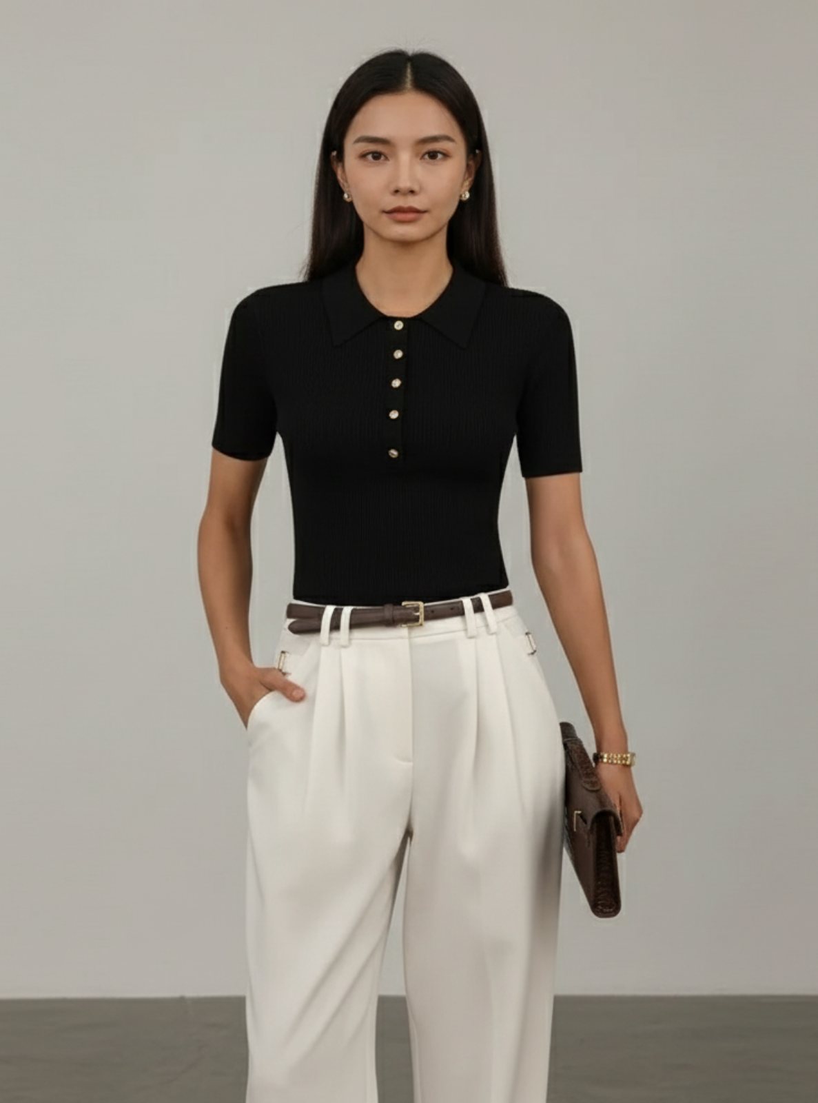 Woman wearing a black polo shirt and white pants against a gray background