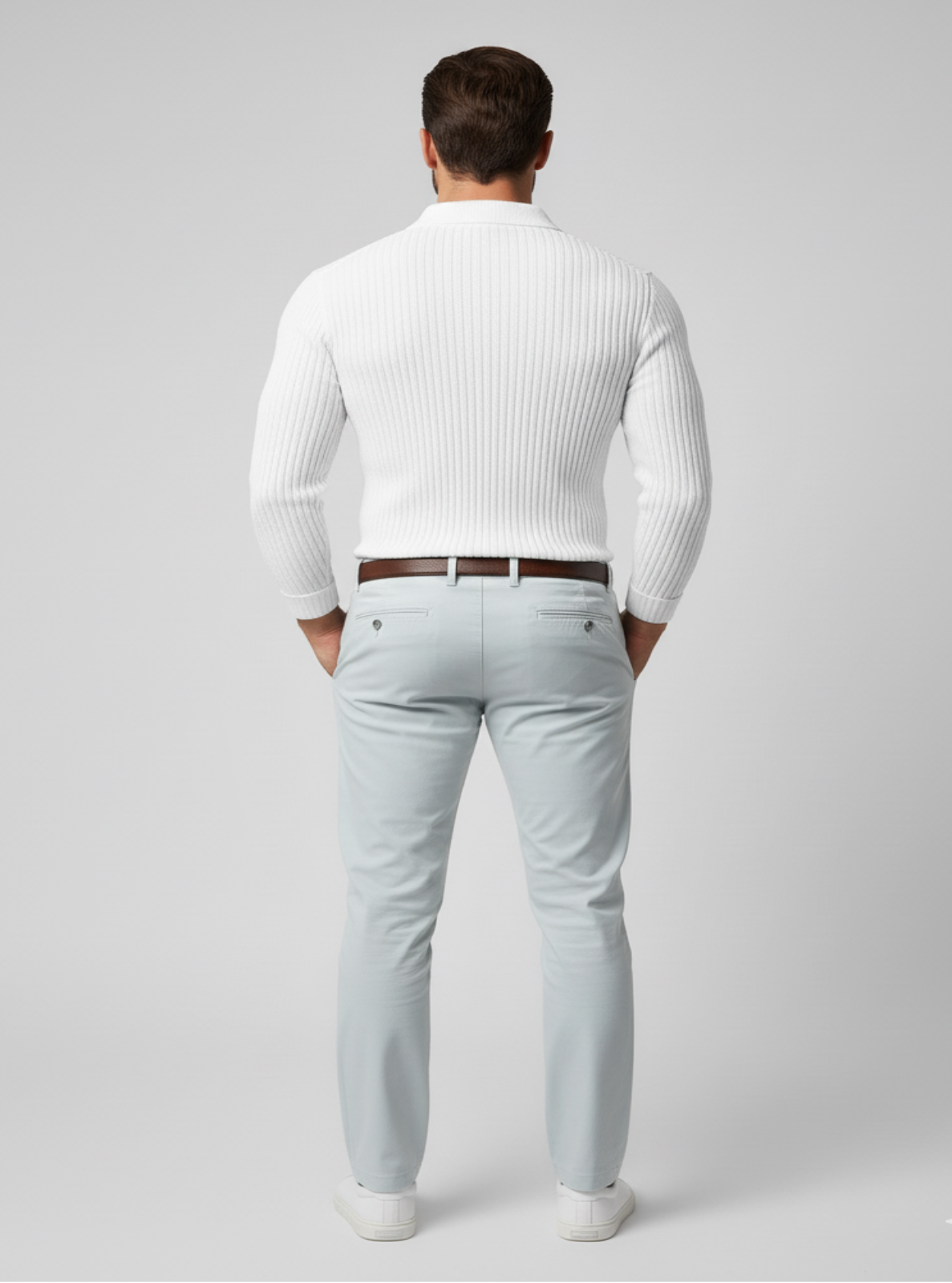 Man wearing a white ribbed sweater and light gray pants on a plain background