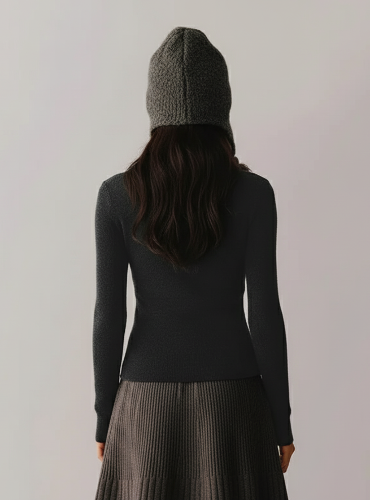 Person wearing a dark gray knit beanie and long-sleeve top with a plain background