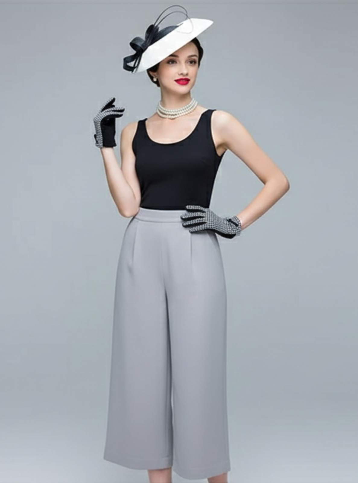 Woman in black top and gray wide-leg pants with a white hat on a gray background