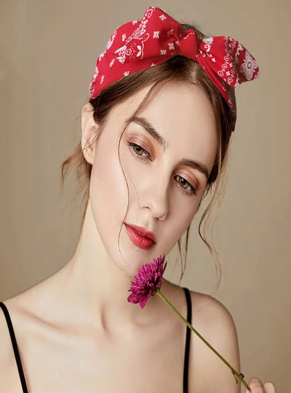 Woman wearing a red bandana with floral patterns, holding a purple flower against a beige background