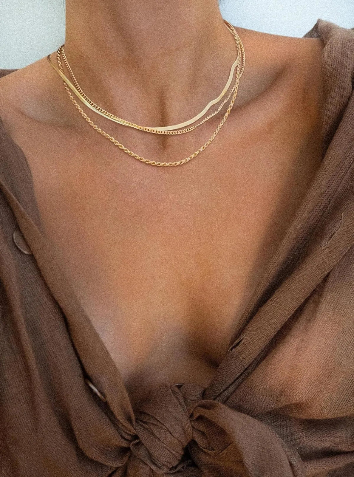 Gold necklace on a person wearing a brown top