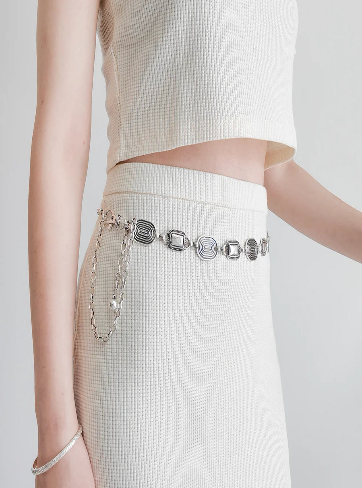Person wearing a white outfit with a silver belt on a plain background