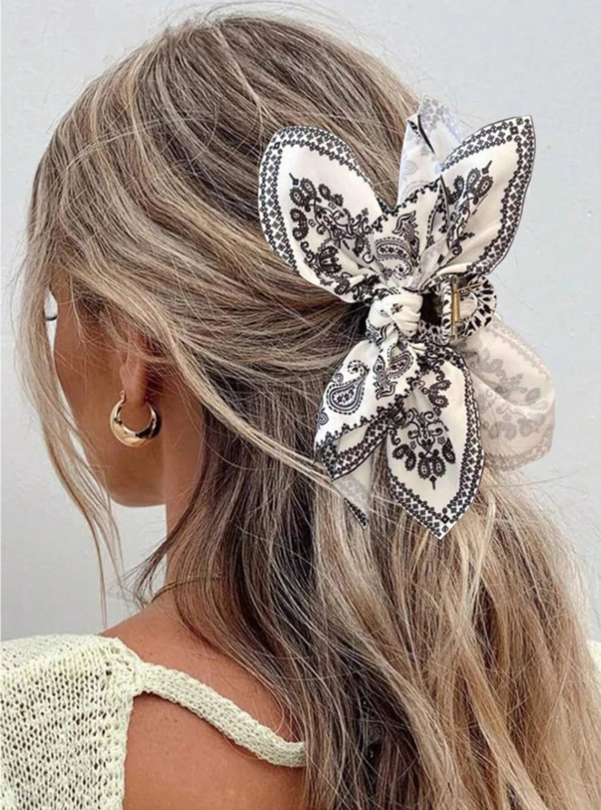 Woman with decorative hair bow and hoop earrings on a plain background