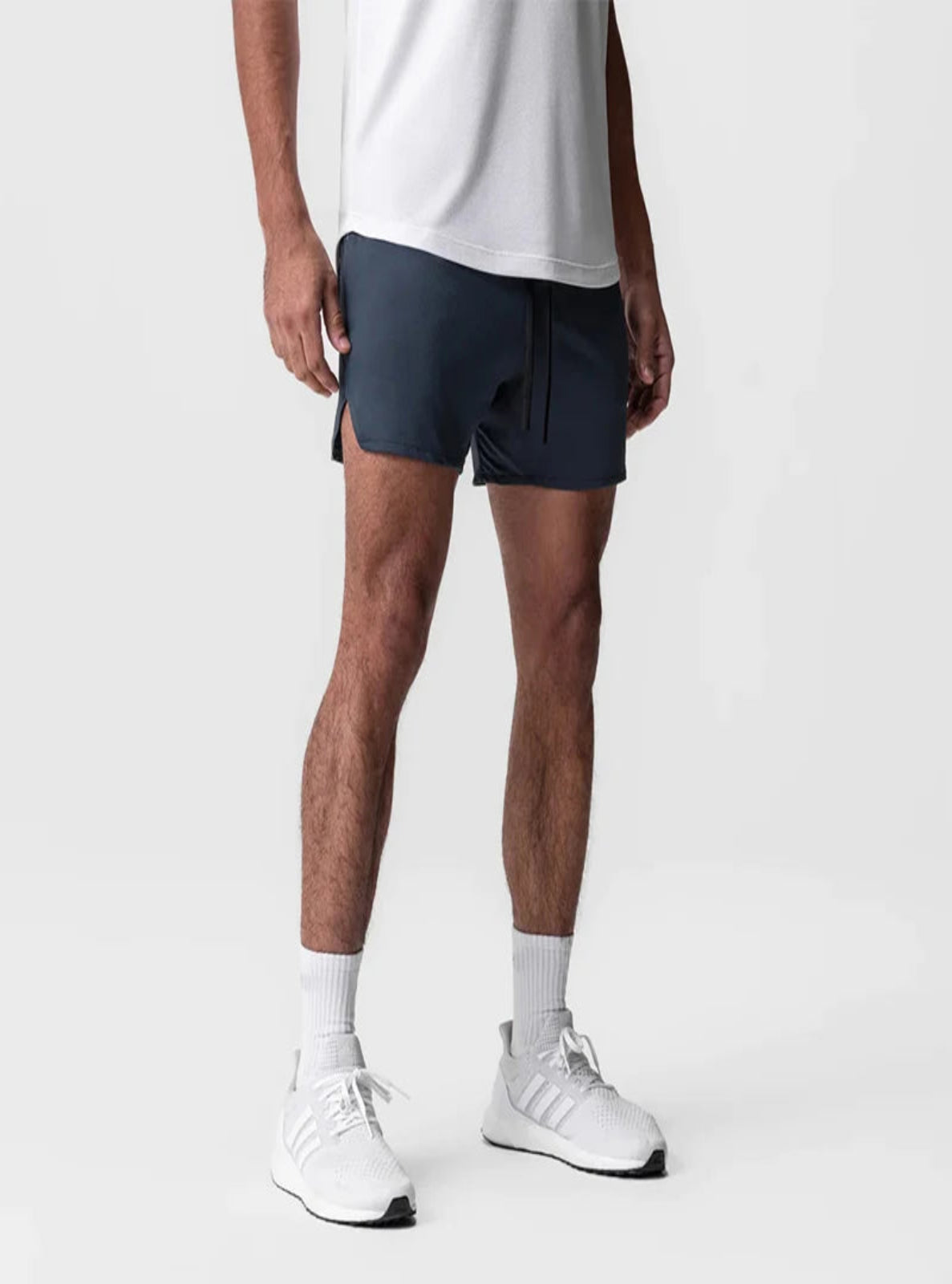 Person wearing navy shorts, white shirt, white socks, and white sneakers on a light gray background