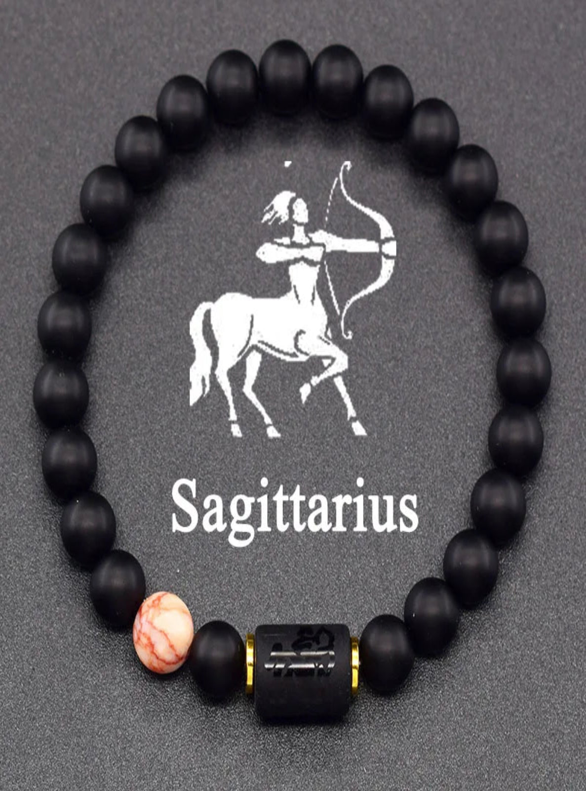 Black beaded bracelet with a pink accent bead and Sagittarius symbol on a dark background