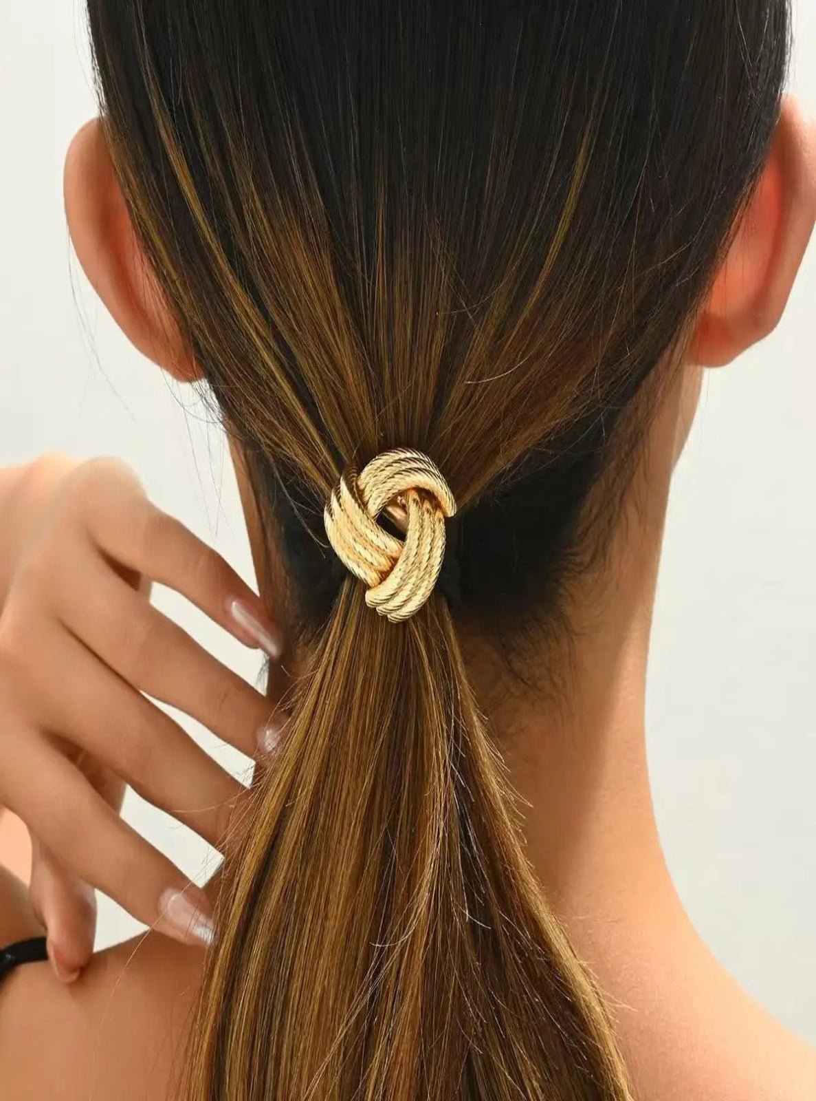 Gold hair tie in a ponytail with a neutral background