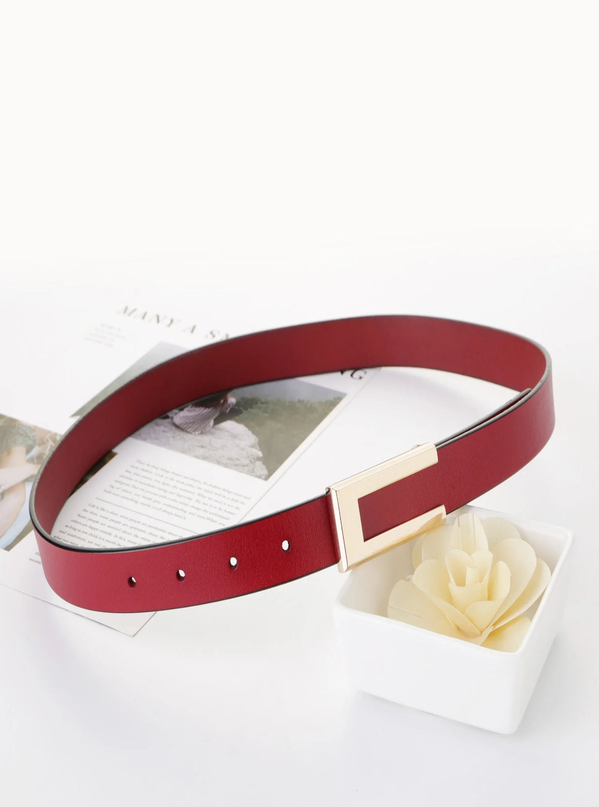 Red belt with a gold buckle on a white surface with a white rose.