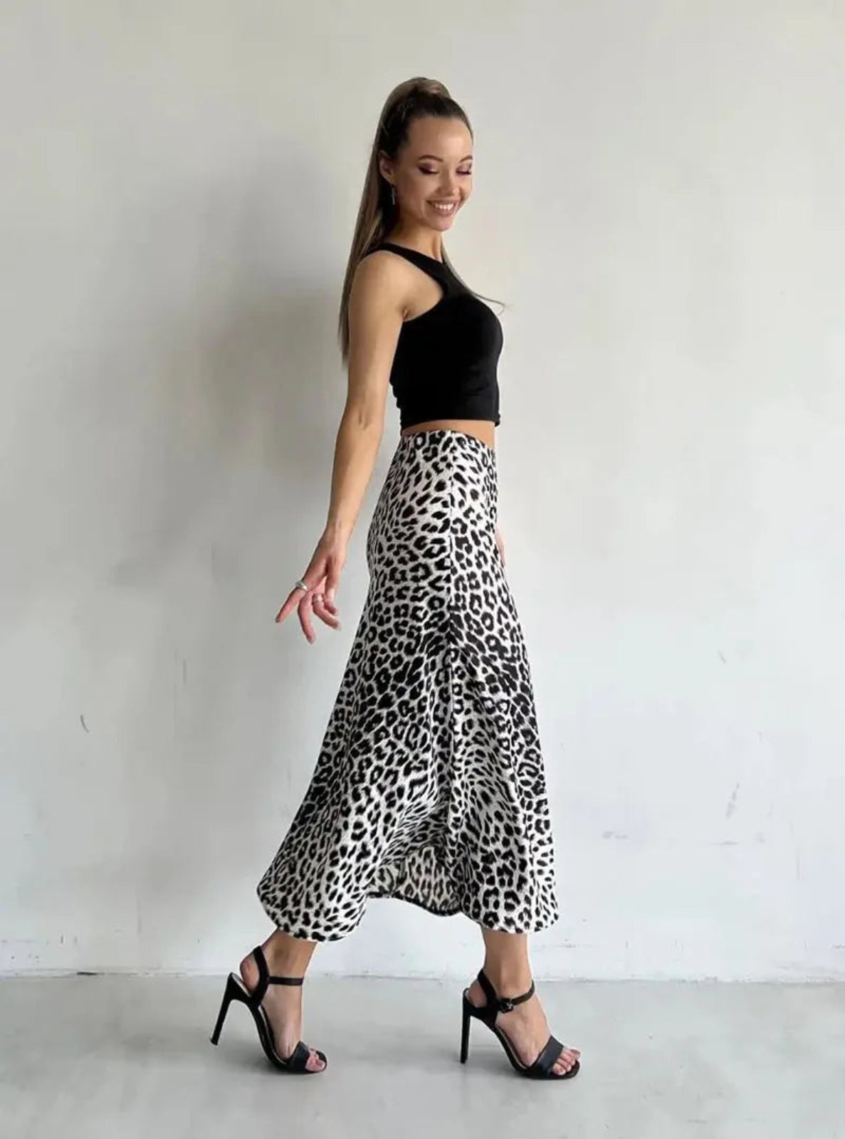 Woman wearing a black top and leopard print skirt against a white background