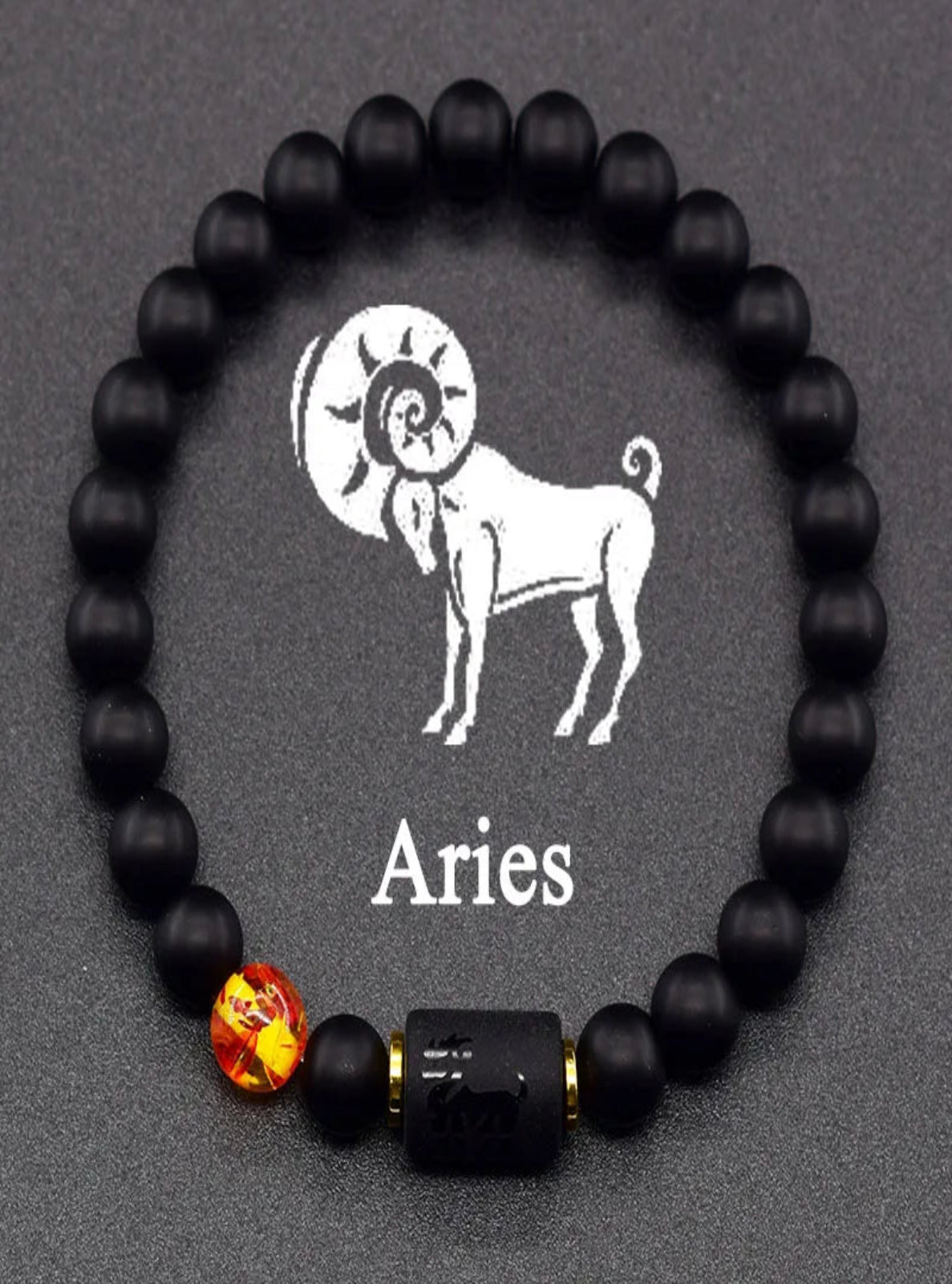 Black beaded bracelet with Aries symbol and red gemstone on a dark background