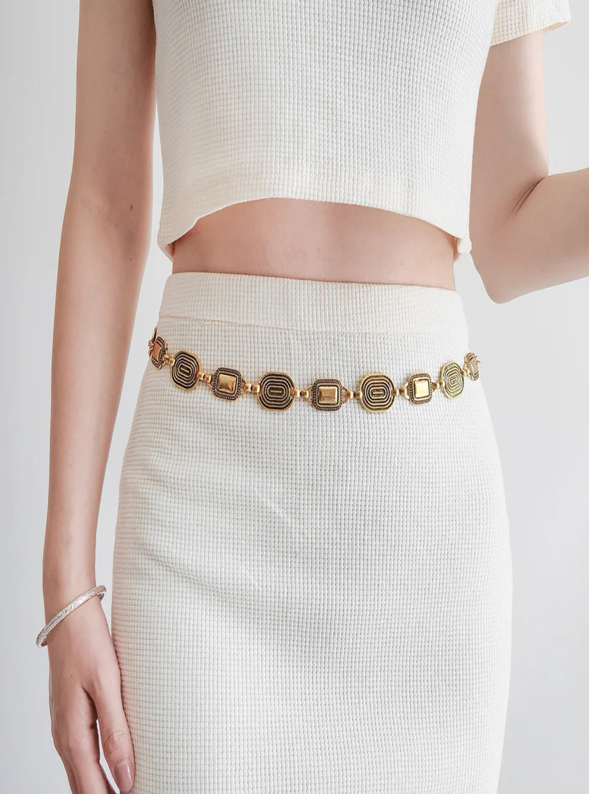 Person wearing a gold belt with a white outfit on a plain background