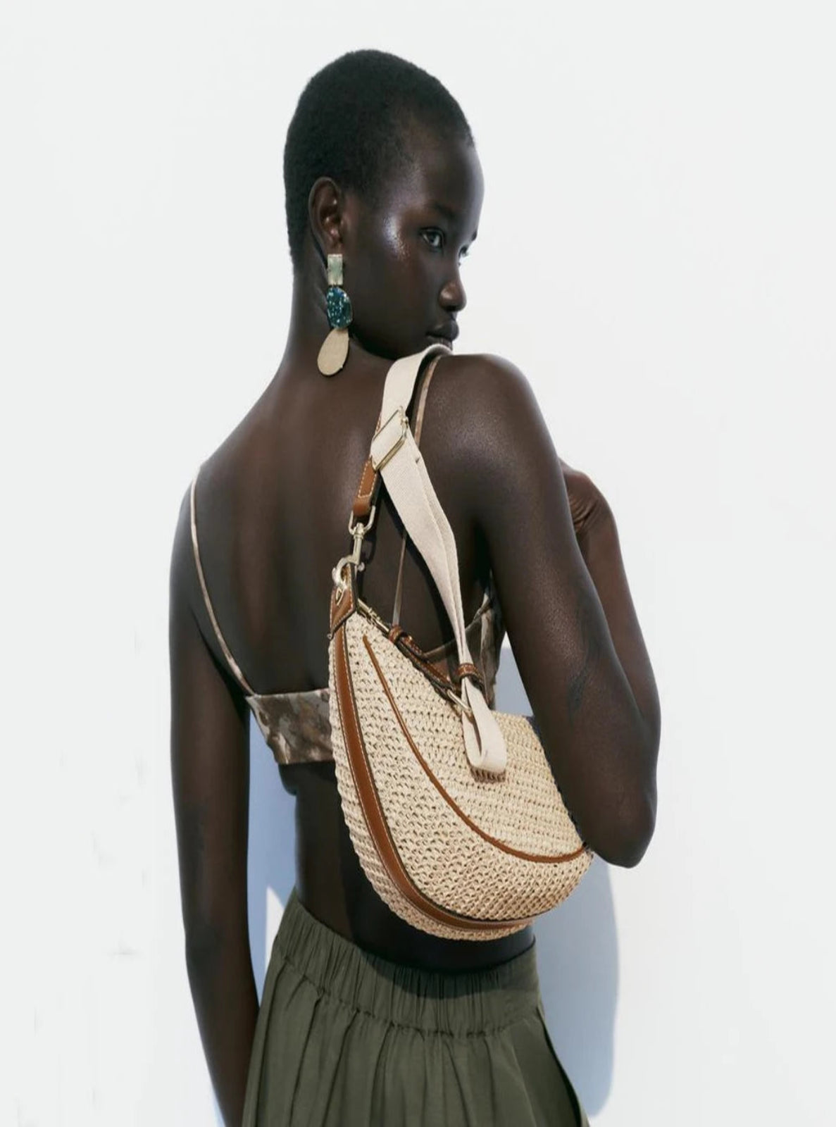 Woman carrying a woven handbag on a plain background