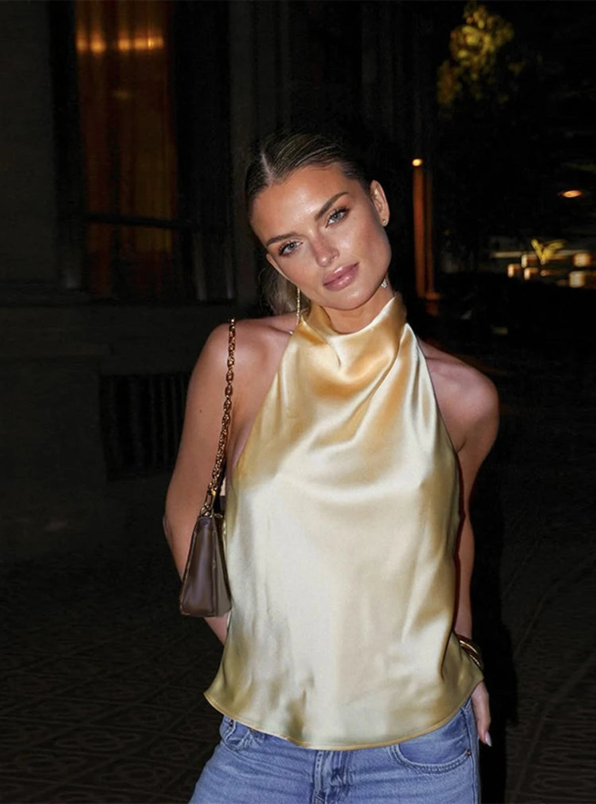 Woman wearing a gold halter neck top and blue jeans at an outdoor event.