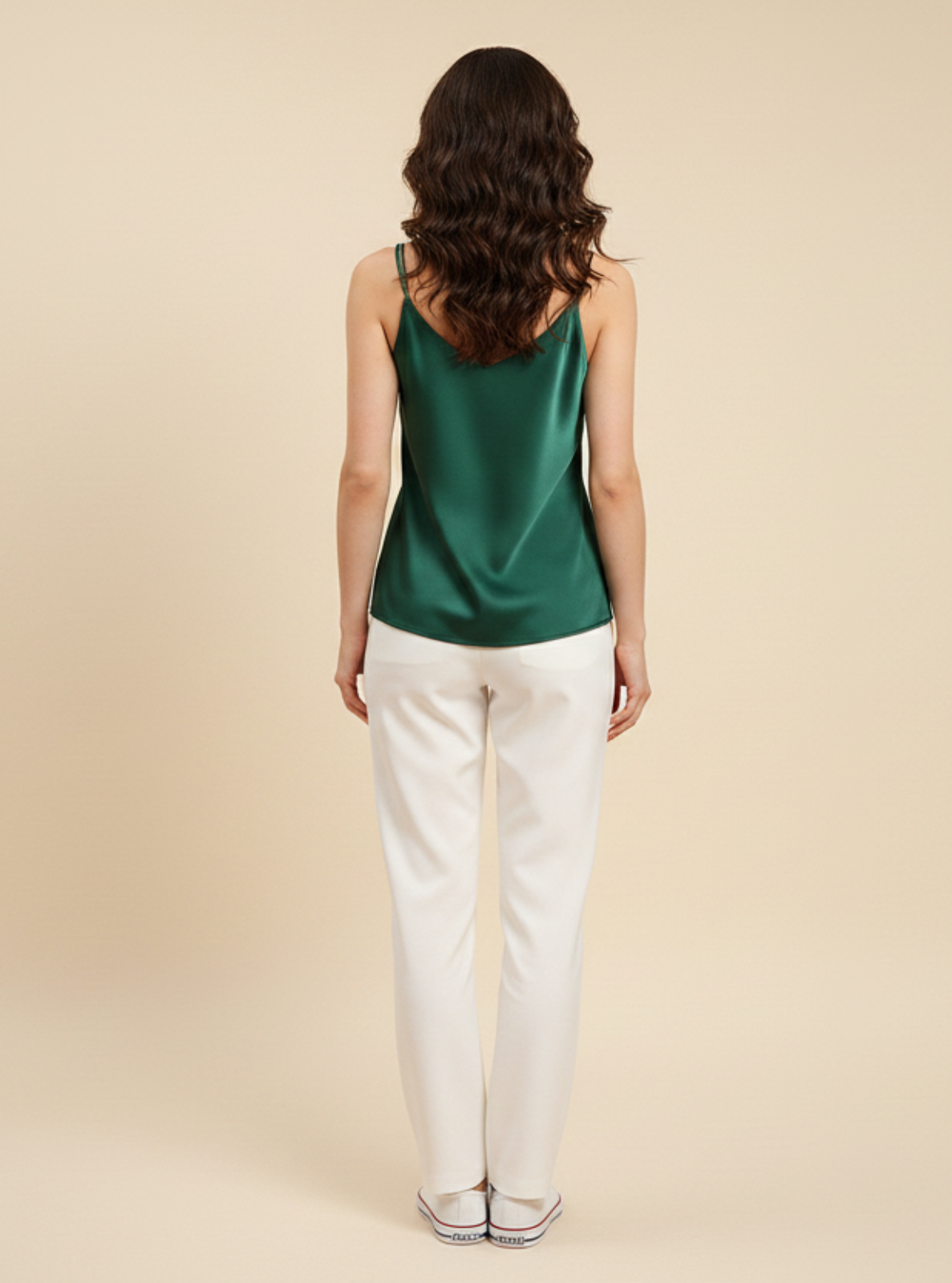 Woman wearing a green top and white pants on a beige background