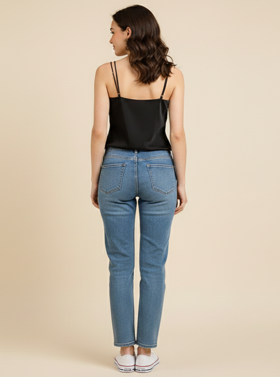 Woman wearing blue jeans and a black top on a beige background