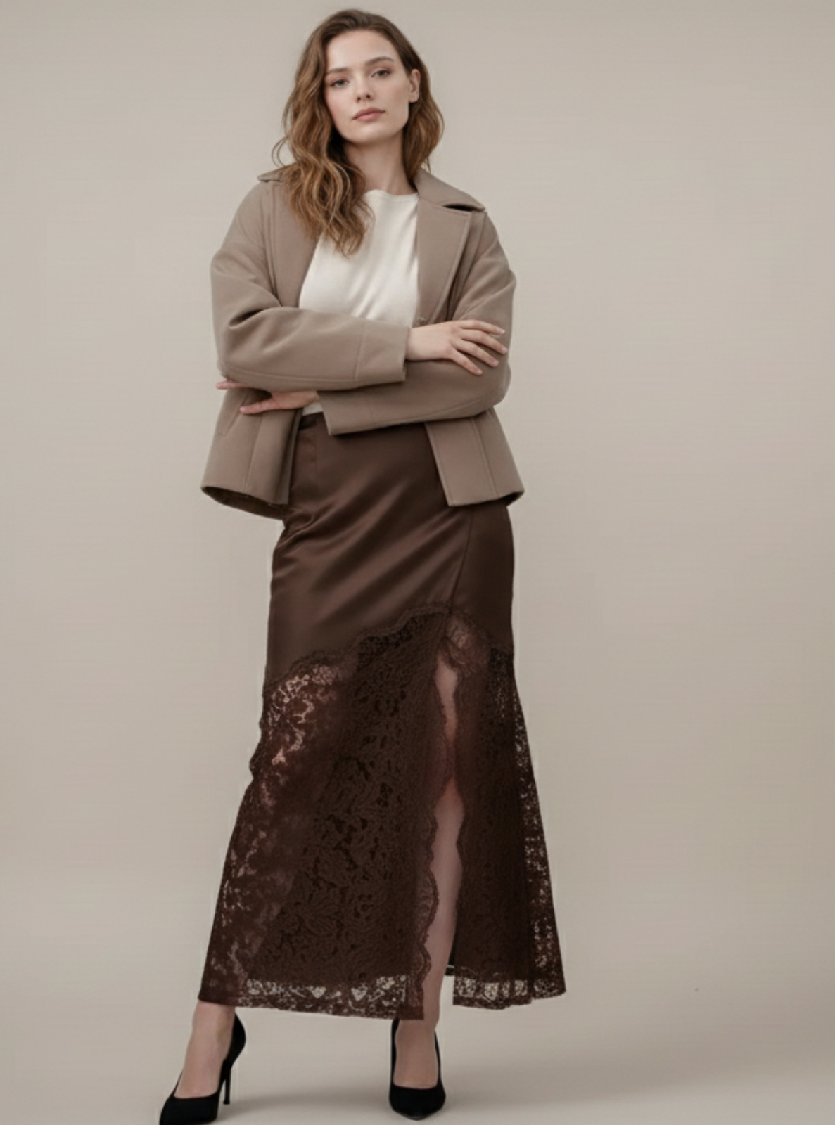 Woman wearing a beige jacket and brown lace skirt against a plain background
