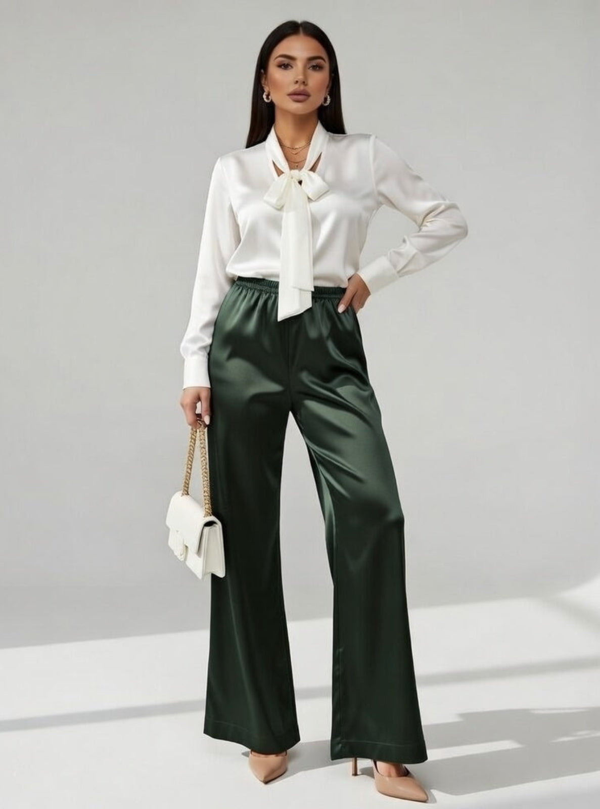 Woman wearing a white blouse and green pants against a gray background