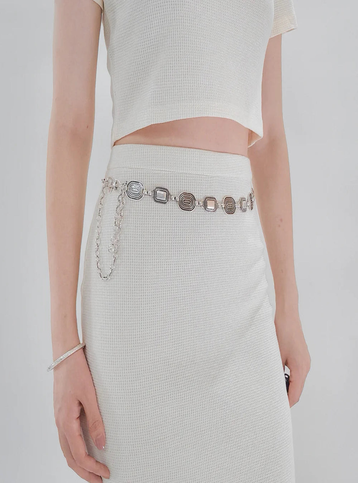 Person wearing a white outfit with a silver belt on a plain background