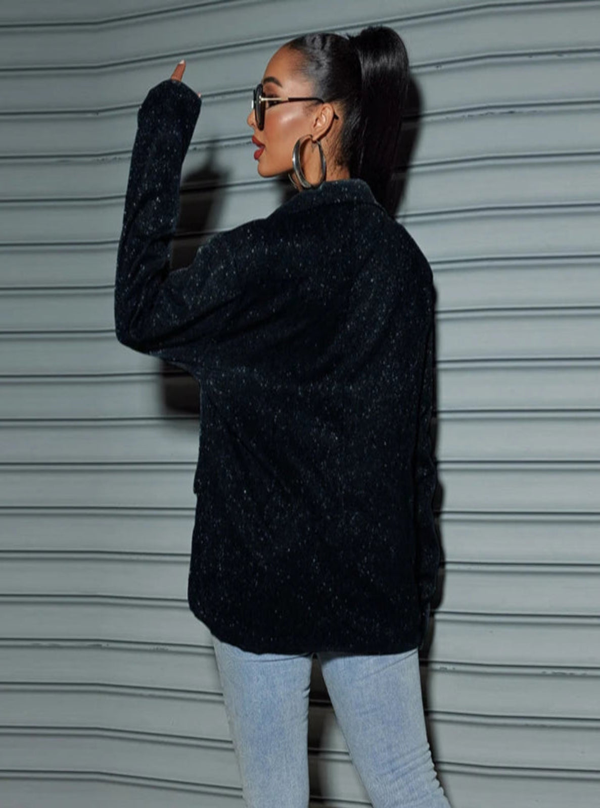 Person wearing a black textured jacket and light blue jeans against a gray background
