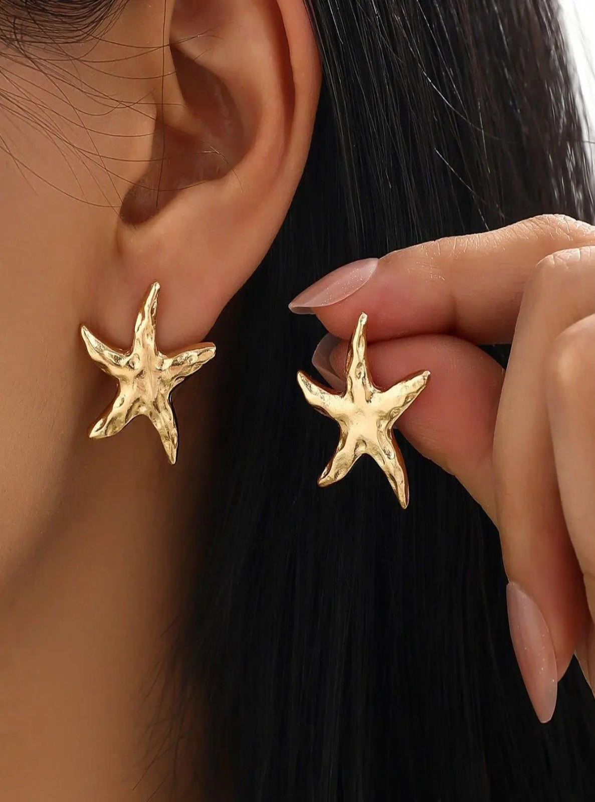 Gold starfish earrings being worn and held by a hand.