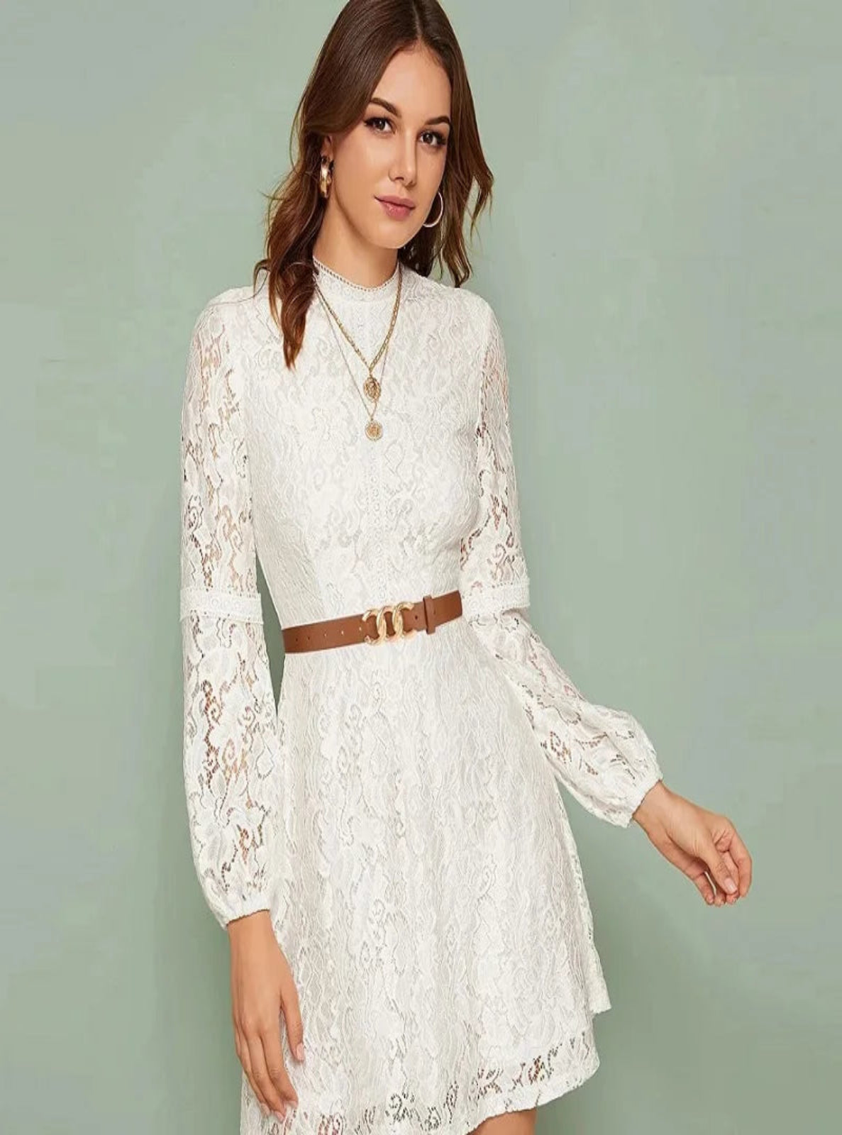 Woman wearing a white lace dress with a brown belt against a light green background