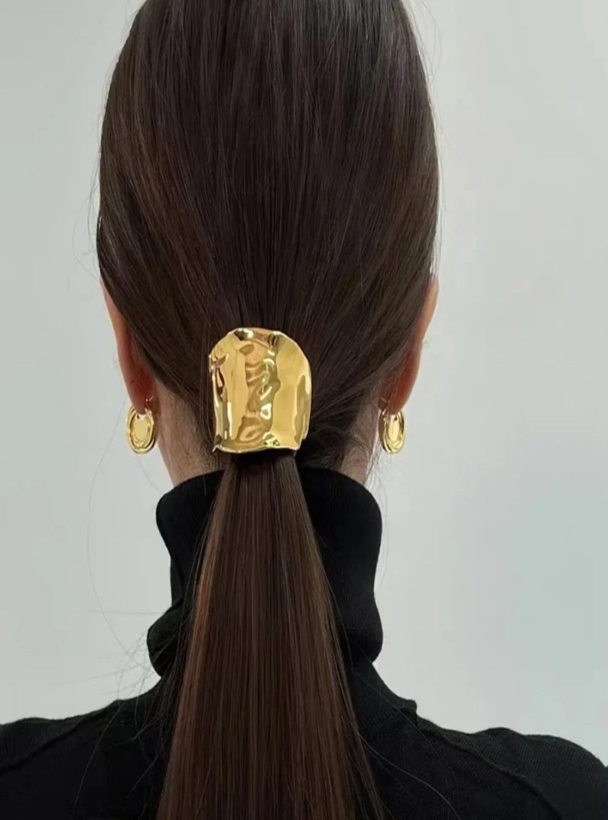Person with a gold elastic hair accessory and earrings on a plain background