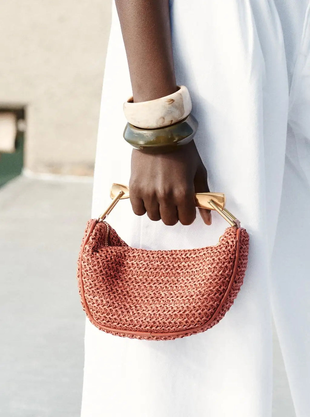 Person holding a red woven handbag with gold handles against a neutral background
