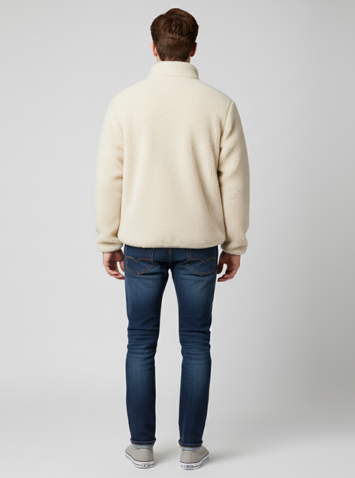 Man wearing a cream sweater and blue jeans on a white background