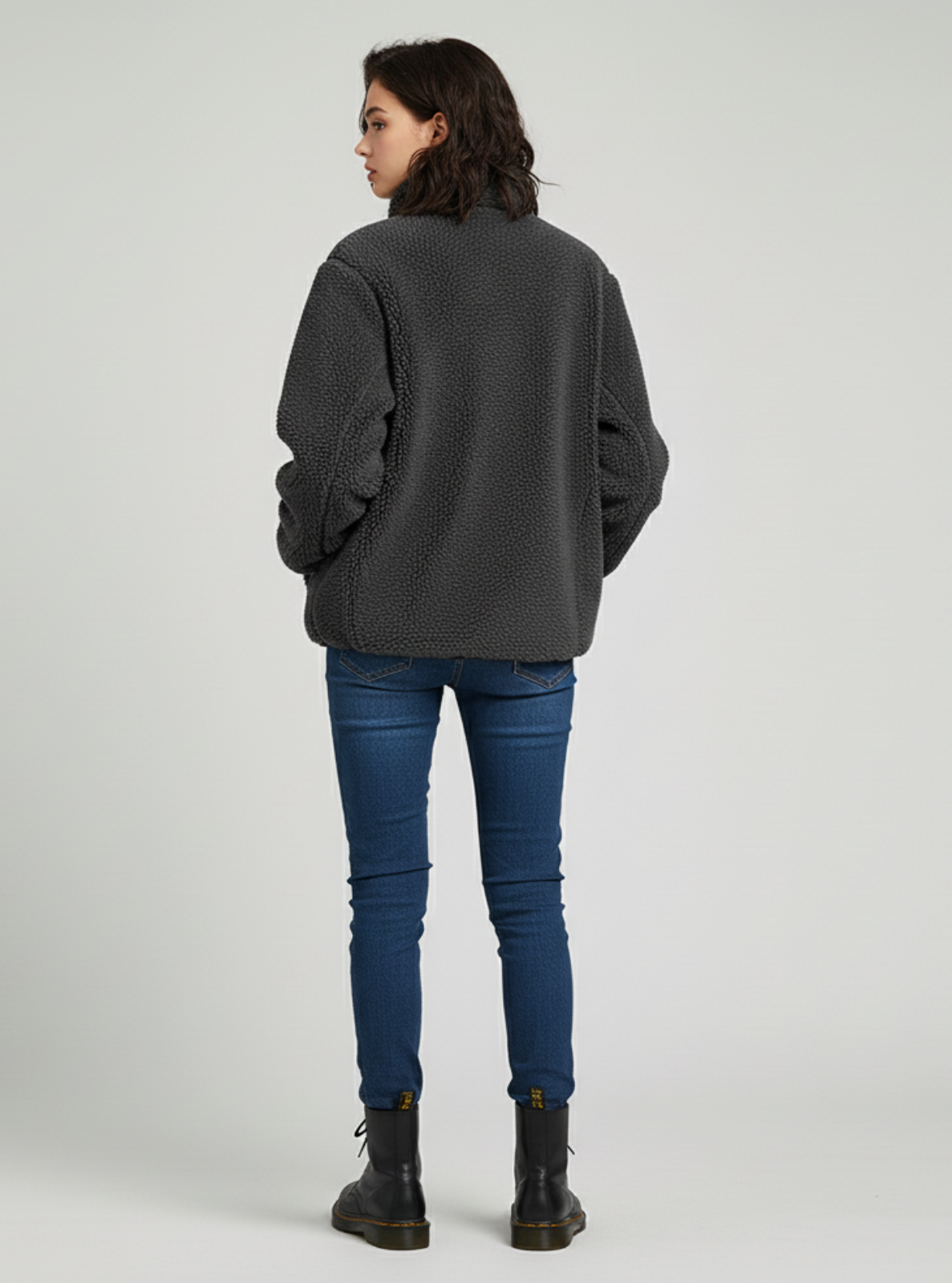 Person wearing a gray sweater, blue jeans, and black boots on a light gray background