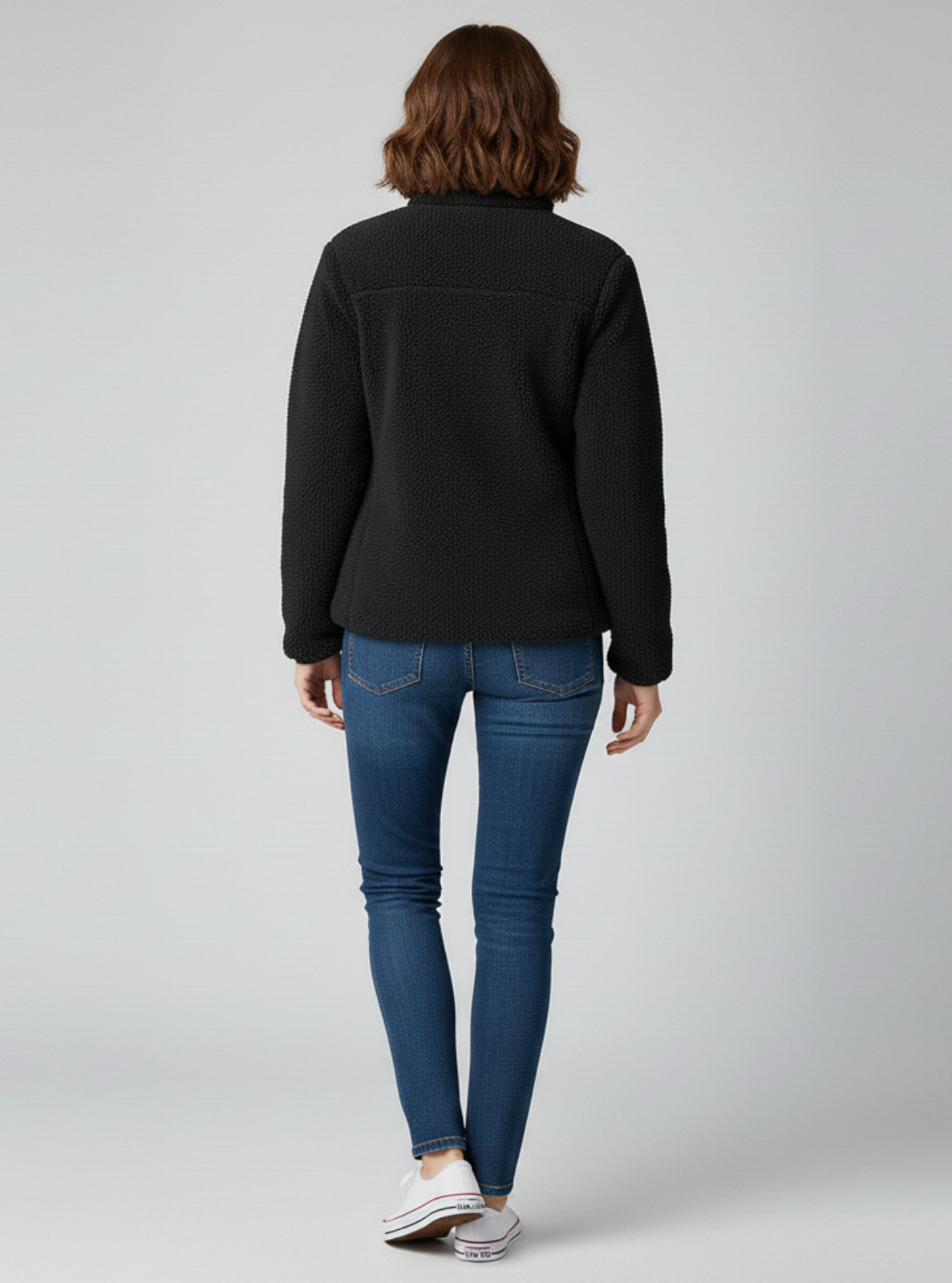 Person wearing a black jacket and blue jeans on a gray background