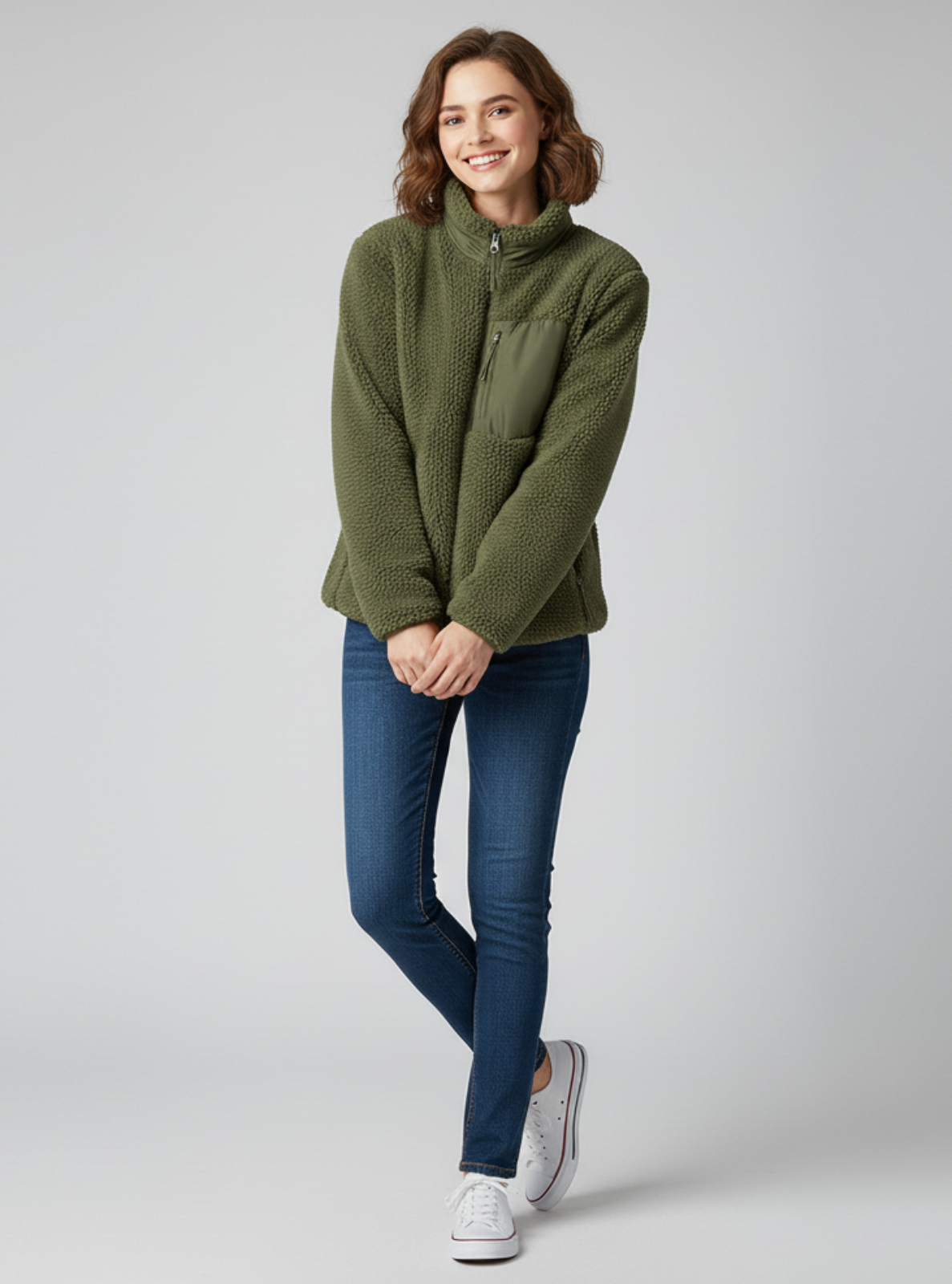 Woman wearing a green textured jacket and blue jeans on a gray background