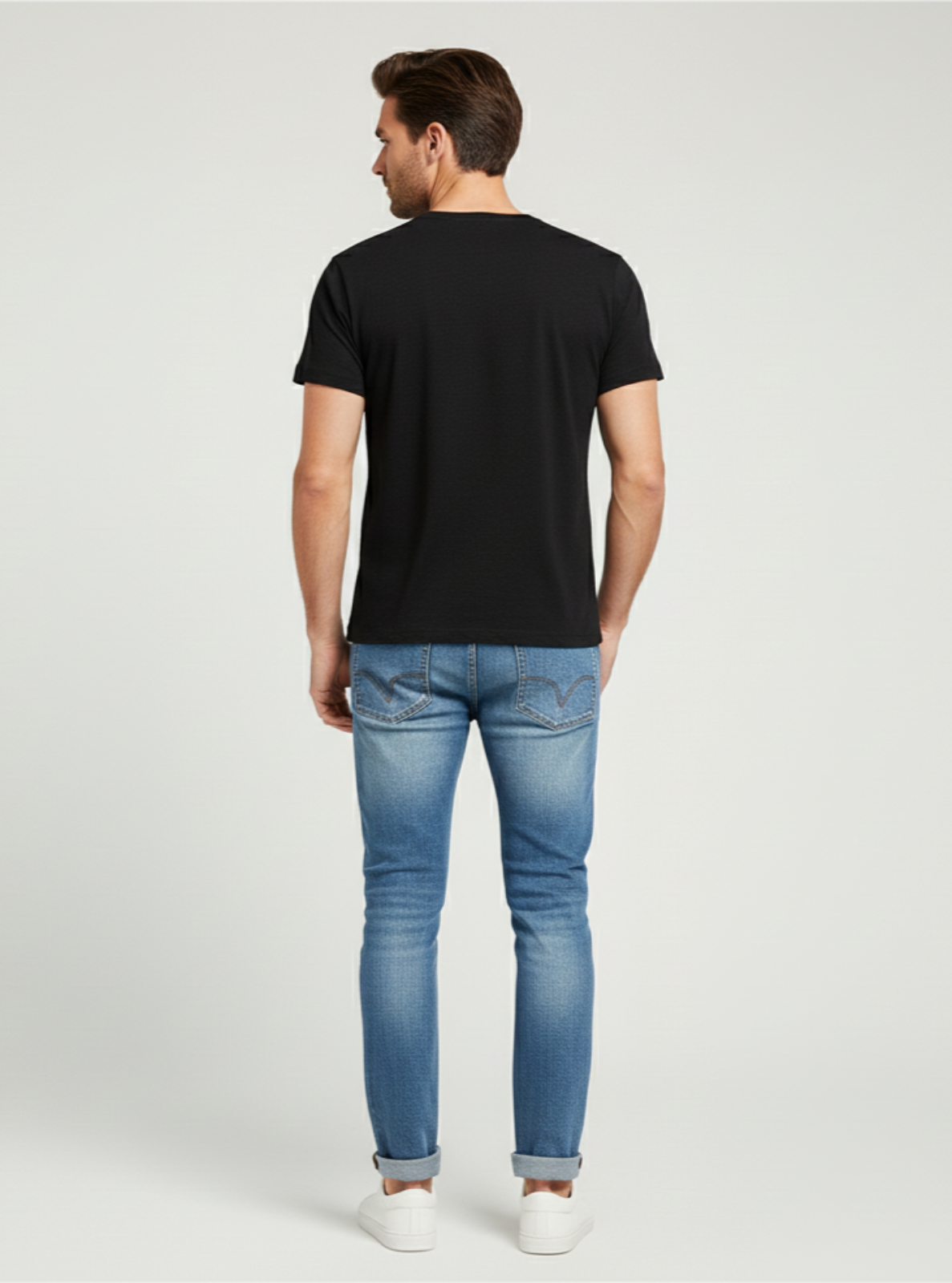 Man wearing a black t-shirt and blue jeans on a light gray background