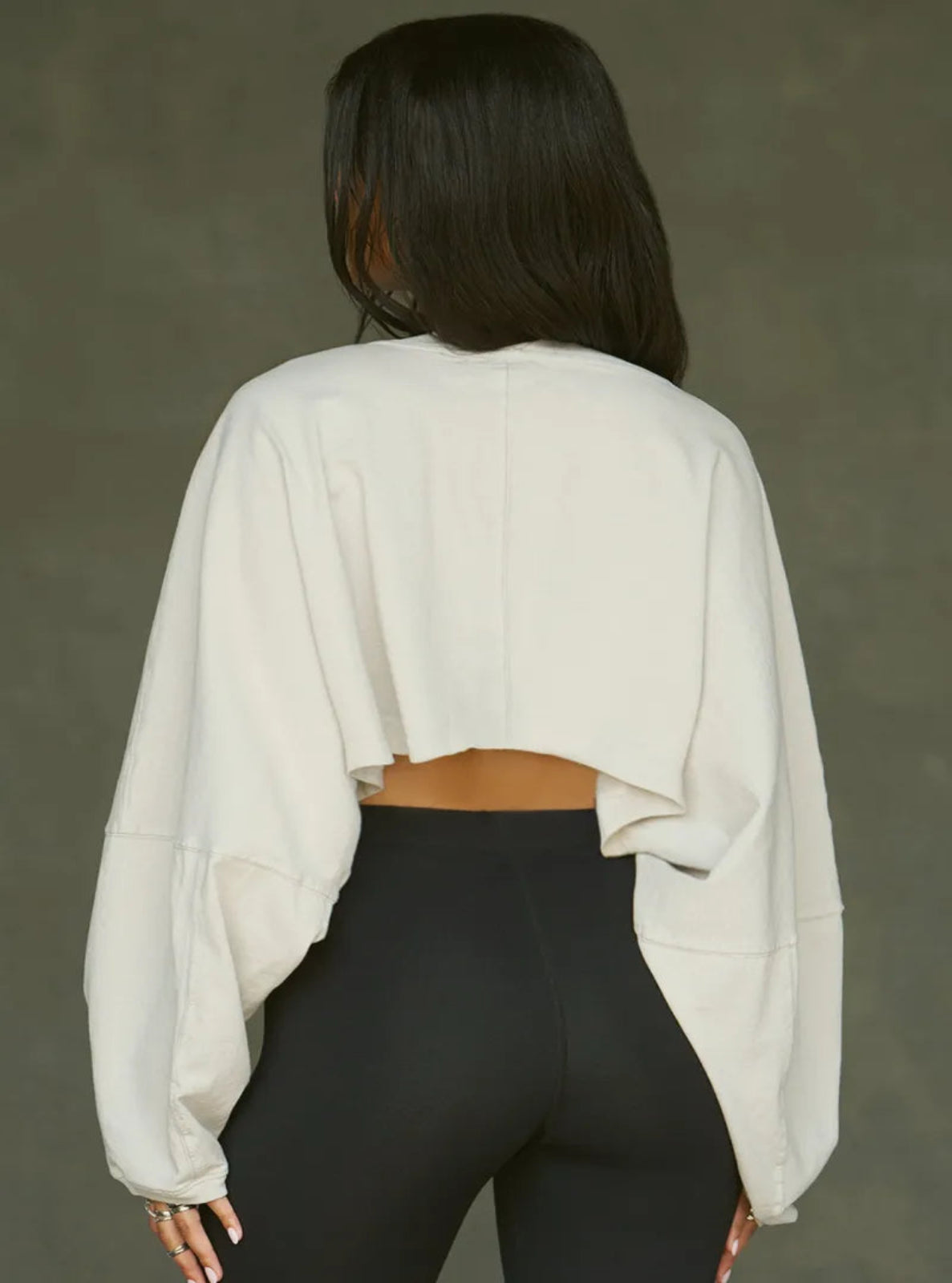 Person wearing a beige sweater and black leggings against a gray background