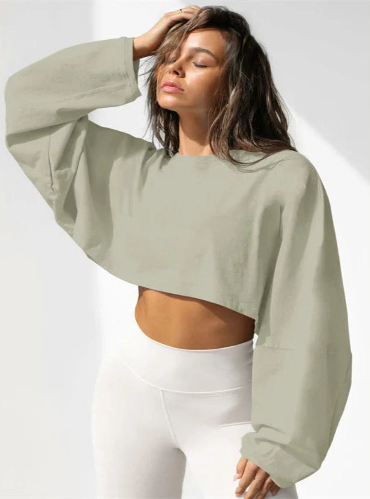 Woman wearing a light green oversized sweatshirt and white pants on a white background