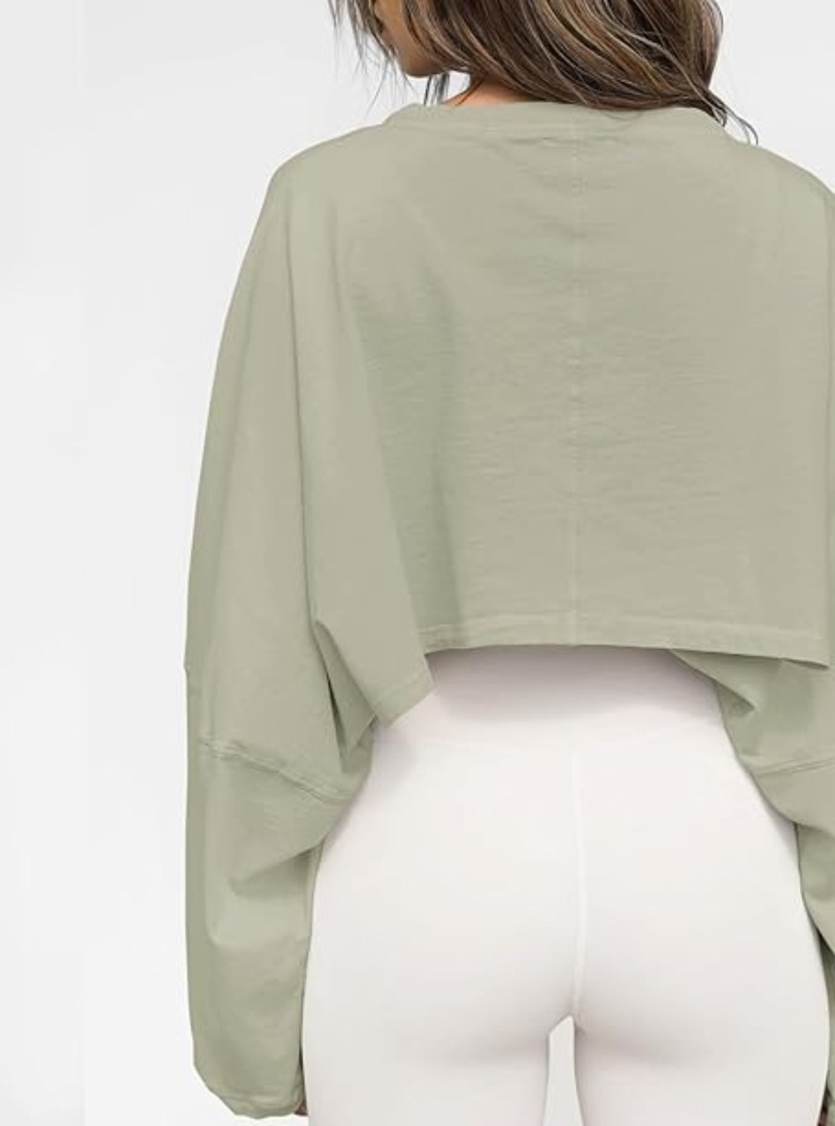 Person wearing a green long-sleeve top and white pants on a white background