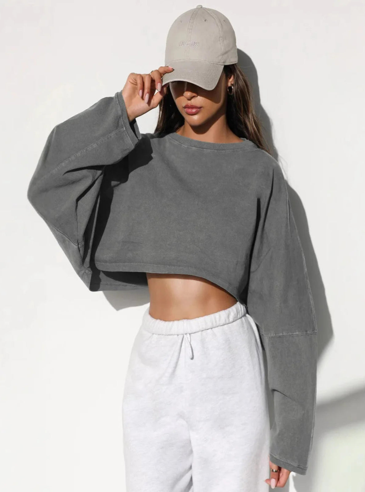 Person wearing a gray cropped sweatshirt and white pants against a white background