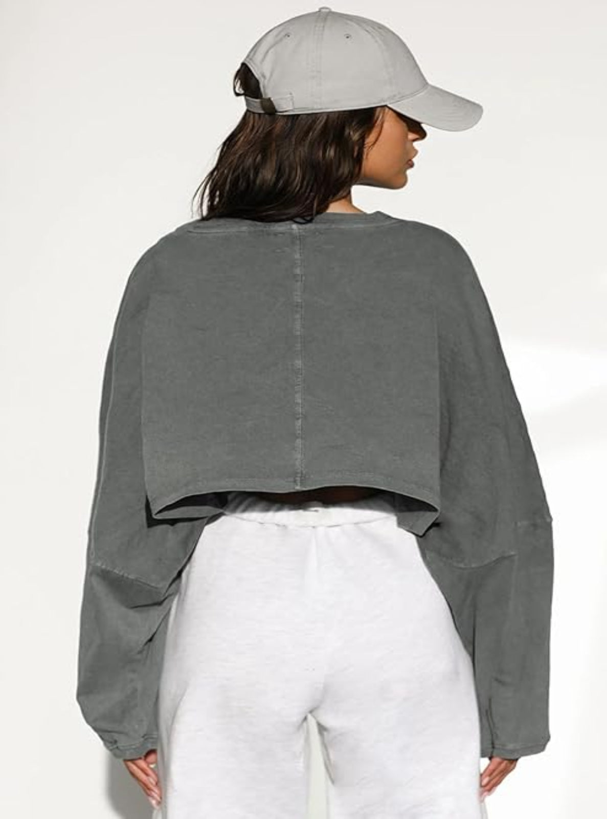 Person wearing a gray cropped sweatshirt and white pants against a white background