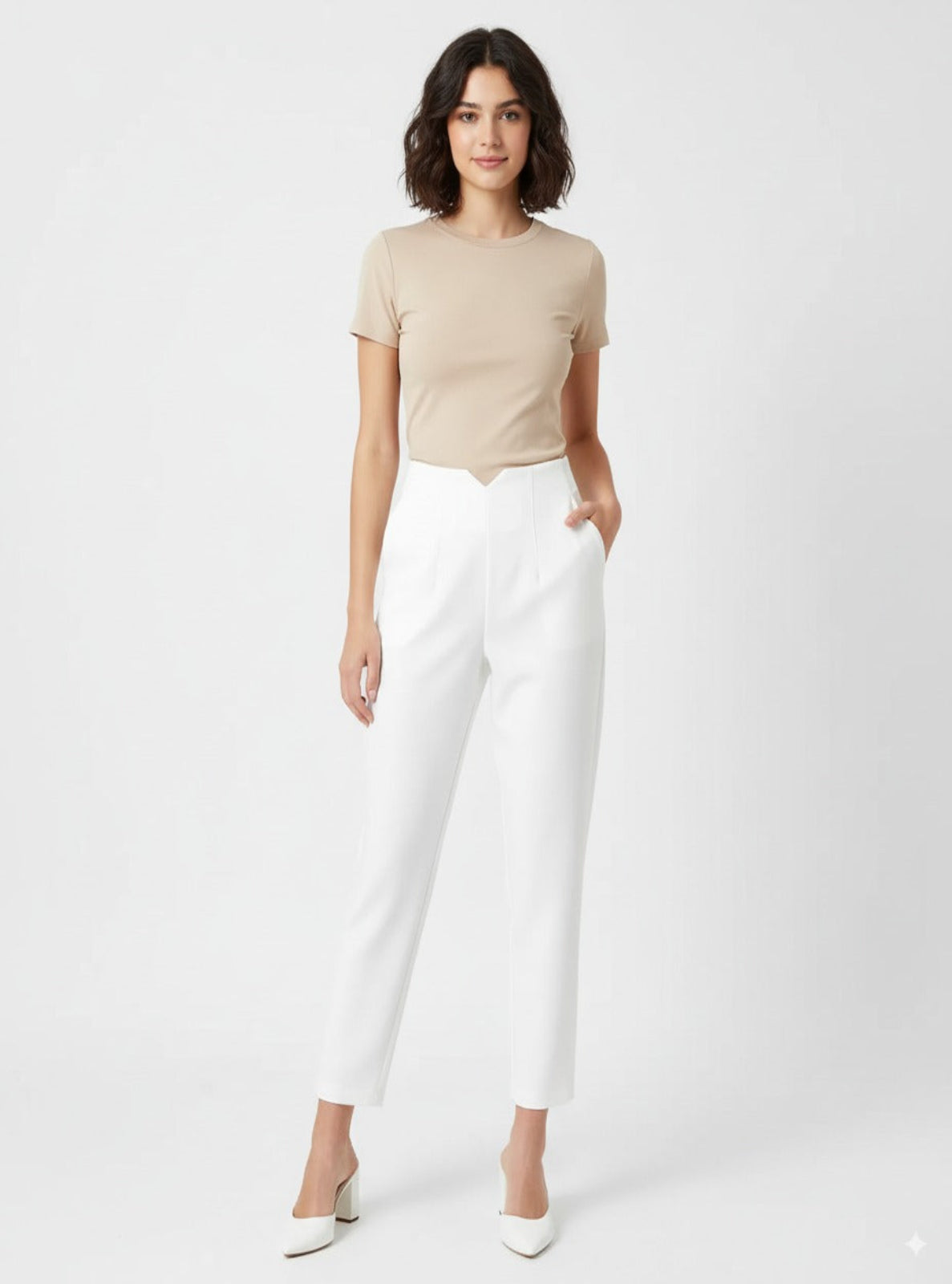 Woman wearing a beige top and white pants on a plain background