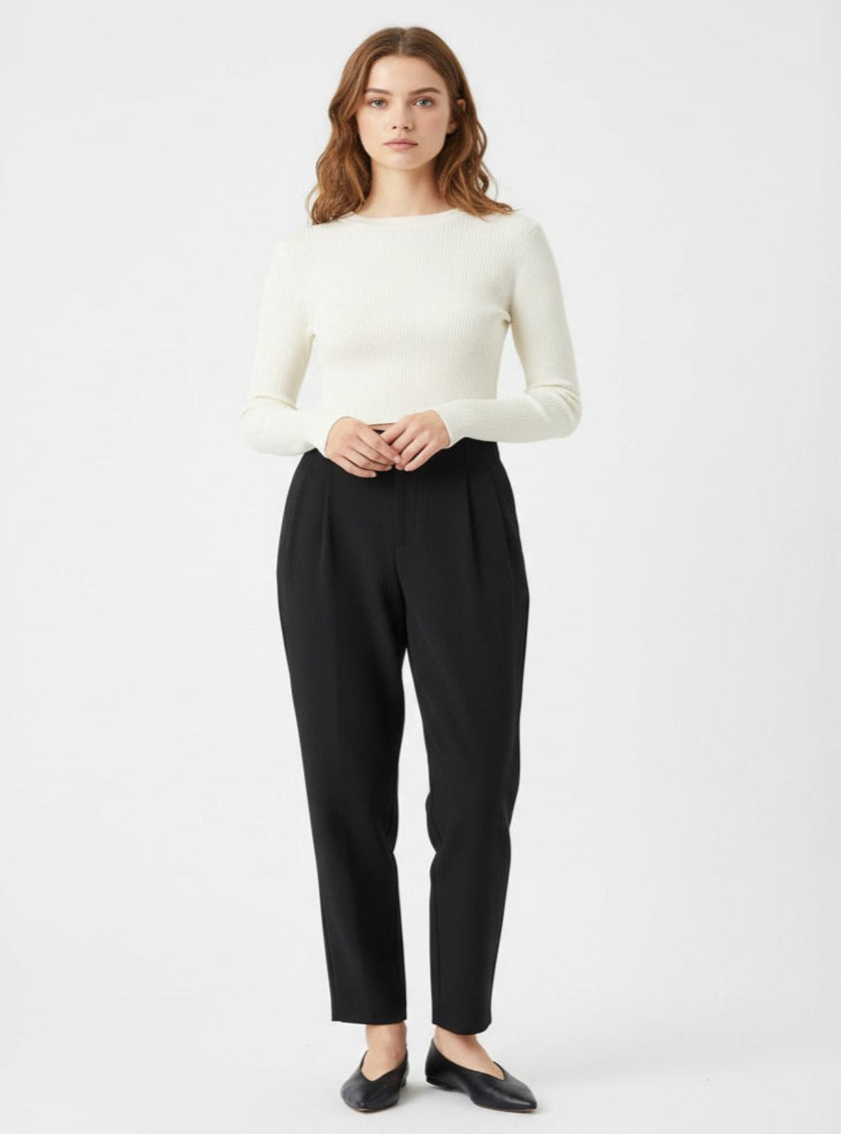 Woman wearing a white sweater and black pants on a light gray background