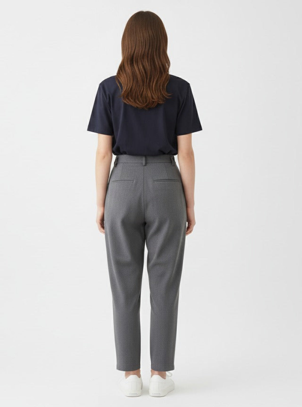 Person wearing a navy shirt and gray pants on a white background