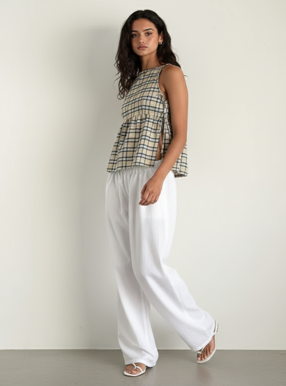 Woman wearing a checkered top and white pants against a plain background