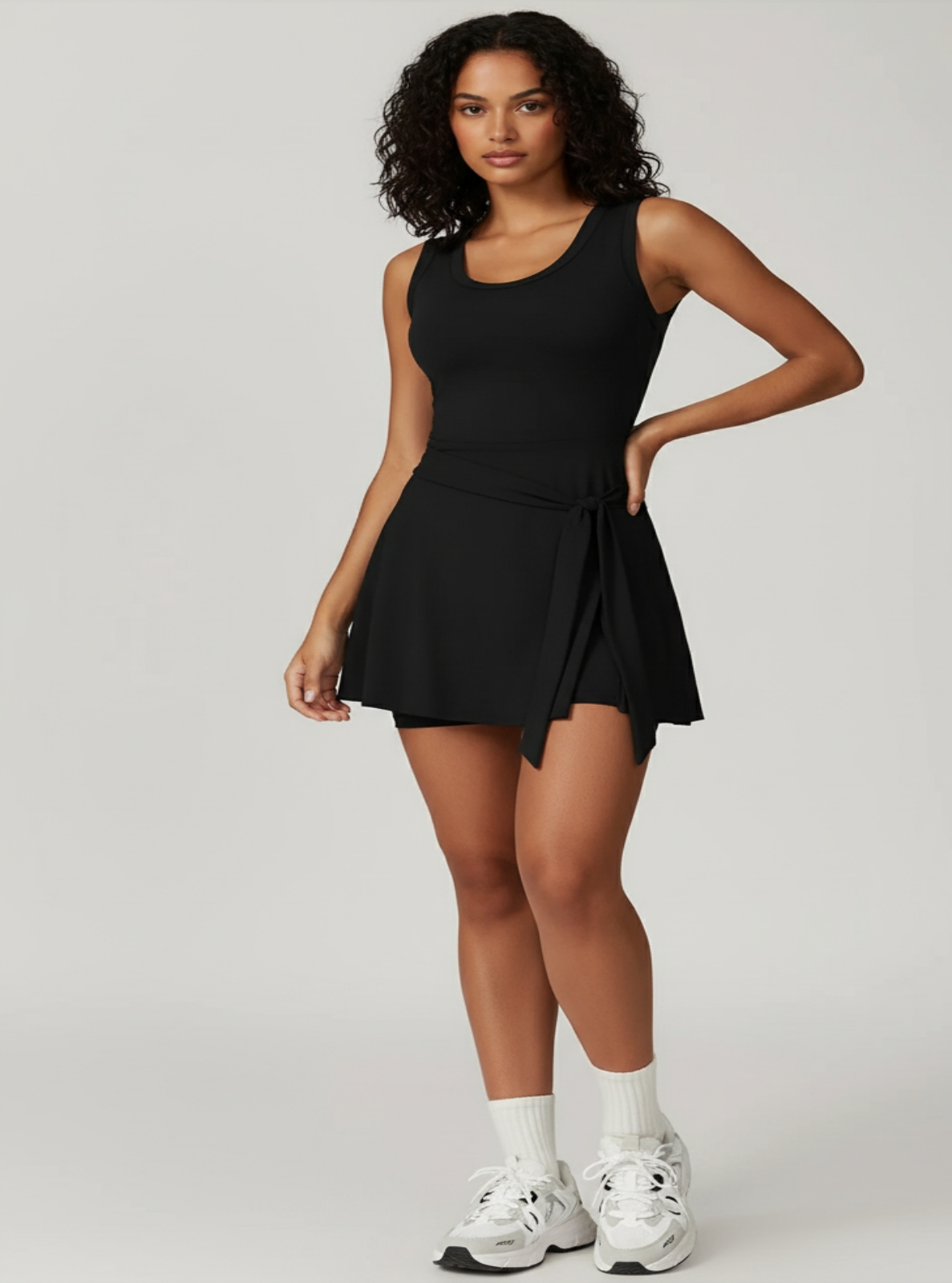 Woman wearing a black dress with white sneakers on a light gray background