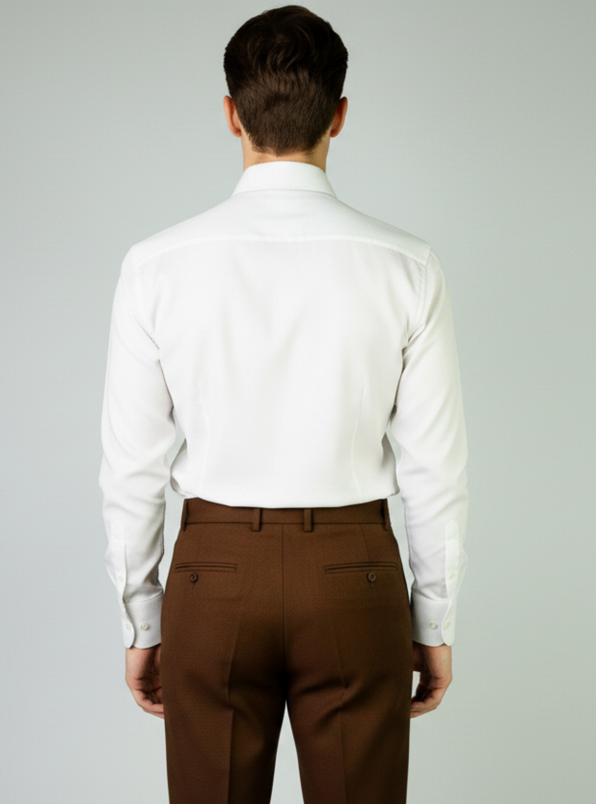 Man wearing a white dress shirt and brown pants on a plain background