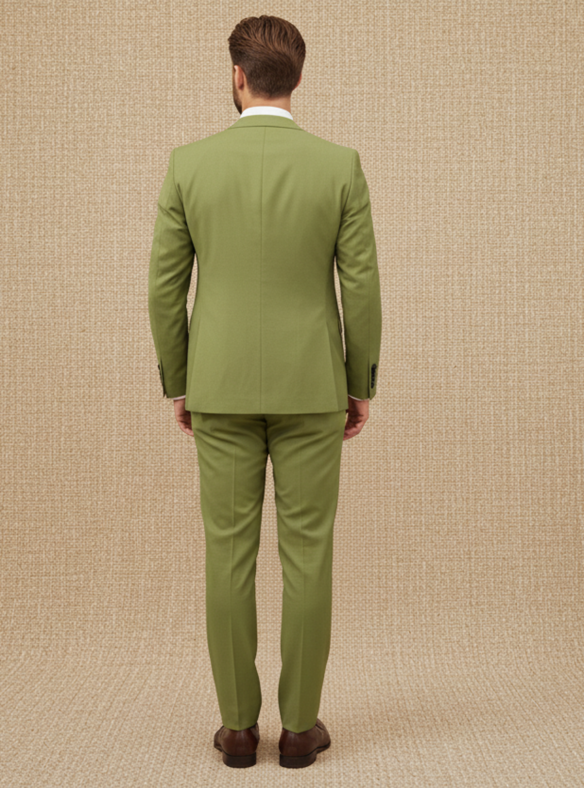 Man wearing a green suit standing against a beige textured wall.